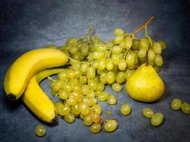 A large bunch of grapes with bananas and pears on a black background.   Still life photo