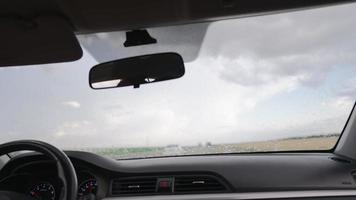 vista de dentro de um carro dirigindo ao longo da estrada durante a chuva, os limpadores de carro funcionam. conceito de veículos e transporte. ninguém. video