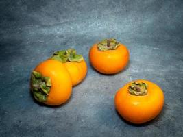 Four persimmons on a black background. Persimmon varieties Chamomile.   Big ripe tasty fruits on the table. photo