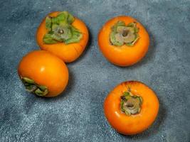 Four persimmons on a black background. Persimmon varieties Chamomile.  Big ripe tasty fruits on the table. View from above photo