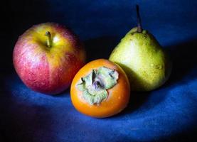 Bodegón de frutas. manzana, caqui y pera sobre un fondo negro. manzanilla caqui. gala de manzana alimentación saludable. vegetarianismo. foto