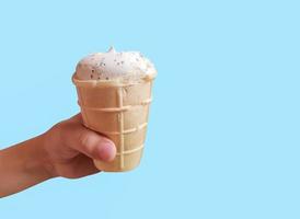 Fresh white ice cream in waffle cup in kid's hand on blue background photo