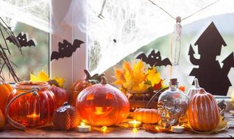 Festive decor of the house on the windowsill for Halloween - pumpkins, Jack o lanterns, skulls, bats, cobwebs, spiders, candles and a garland - a cozy and terrible mood photo