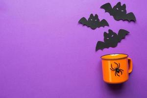 Orange mug on a purple background with terrible Halloween decorations. The concept of the Halloween holiday. Drink, fun, party. Copy space, mock up, flatly photo