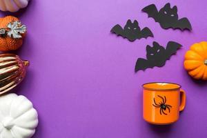 Orange mug on a purple background with terrible Halloween decorations. The concept of the Halloween holiday. Drink, fun, party. Copy space, mock up, flatly photo