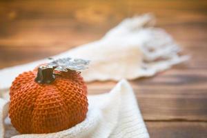 Orange pumpkin wrapped in a warm white plaid with lights of garlands on a wooden table with copyspace. Autumn mood, halloween, harvest, thanksgiving, home decor and cozy. Selective focus photo