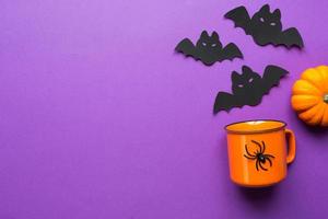 Orange mug on a purple background with terrible Halloween decorations. The concept of the Halloween holiday. Drink, fun, party. Copy space, mock up, flatly photo