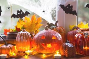 Festive decor of the house on the windowsill for Halloween - pumpkins, Jack o lanterns, skulls, bats, cobwebs, spiders, candles and a garland - a cozy and terrible mood photo