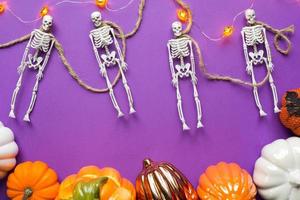 Halloween layout of garland of skeleton on a rope, glowing Jack o Lantern, pumpkins, spiders on a purple background. Flat lay horror and a terrible holiday photo