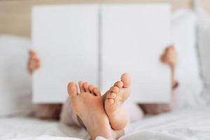 Children bare feet and hands close up Kid reading book in white cozy bed before sleepping night Copy space mock up place for text Rest and holiday in hotel photo