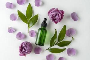 A face serum or essential oil in a green dropper bottle lying on a white background with rose petals around it photo