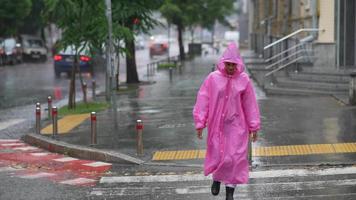 Woman in pink hooded poncho navigates a city street in the rain video