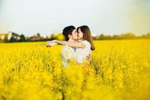 una pareja joven enamorada se abraza y se besa apasionadamente mientras posan contra el campo amarillo de flores, demuestran relaciones verdaderas y devoción. concepto de personas, amor y devoción foto