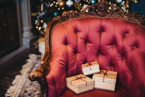 Horizontal picture of wrapped three gift boxes on beautiful royal armchair indoors. Home interior. Celebration, holidays, present concept. Christmas presents decorated with ribbons photo