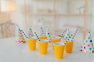 Holiday hats and paper cups with beverage and straws on white table. Festive event. Birthday party celebration concept. Blurred background. Nobody on picture photo