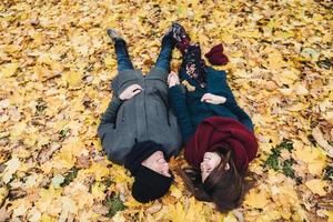 Romantic young couple lie on yellow leaves in park, hold hands together, look at each other with great love, enjoy autumn sunny day. People, relationships, togetherness and romance concept photo