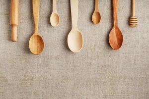 Craft spoons made from different types of wood lie in a row on a hemp burlap fabric. Top view, free space photo