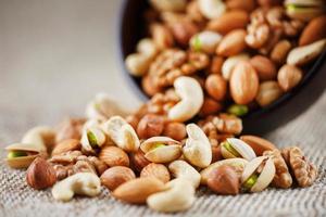 Nuts of various varieties spill out from a wooden plate on a table with a burlap cloth. photo