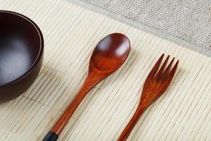 taza vacía de madera oscura, cuchara y tenedor de madera natural sobre un respaldo de bambú claro foto