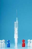 A syringe with a vaccine in the center with a blue and red man with a crowd of whites on a blue background. photo