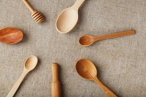 Craft spoons made from different types of wood lie in a row on a hemp burlap fabric. Top view, free space photo