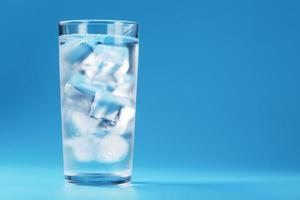 vaso con agua y cubitos de hielo sobre un fondo azul foto