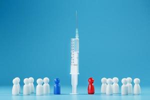 A syringe with a vaccine in the center with a blue and red man with a crowd of whites on a blue background. photo