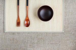 Empty dark wooden cup, spoon and fork made of natural wood on a light bamboo backing photo