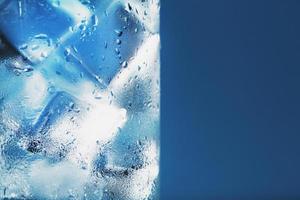 vaso con agua y cubitos de hielo sobre un fondo azul foto