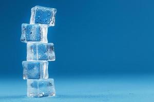 cubos de hielo con torre de gotas de agua en una fila sobre un fondo azul. foto