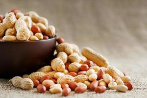 Peanuts in the shell and peeled close-up in cups. Roasted peanuts in their shells and peeled against a brown cloth. photo