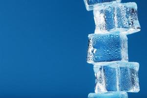 Ice cubes with water drops tower in a row on a blue background.