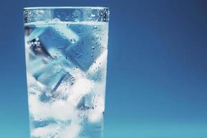 Glass with water and ice cubes on a blue background photo