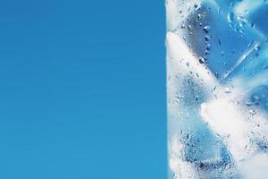 Ice cubes in a glass with refreshing ice water on a blue background. photo