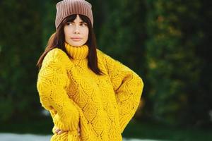 Beautiful European brunette dressed in a yellow woolen sweater and hat outside. The beautiful girl who wears thick stylish autumn clothes in cool weather. photo