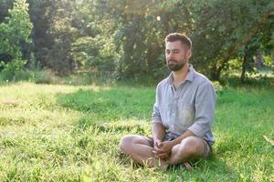 Portrait of young handsome European man in casual clothing sitting on a grass in summer park. photo