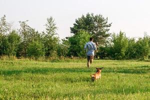 Small funny dog is running by its owner on a grass in park. Active free time by man and dog together. photo