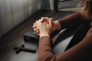 manos juntas en oración a dios junto con la biblia en el concepto cristiano y la religión, la mujer reza en la biblia sobre la mesa foto