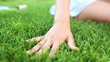 Woman sits outside with laptop touching hands to the green grass video