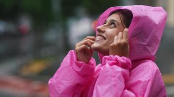 Woman in pink hooded poncho navigates a city street in the rain video