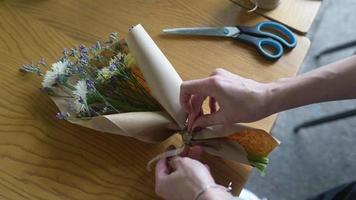 florista embrulha buquê de flores em papel pardo e barbante video