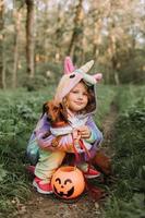 niña riendo y un perro salchicha enano en disfraces de halloween con una canasta de calabaza para dulces al aire libre. una niña con un disfraz de kigurumi de unicornio arcoíris, un perro con un vestido con una falda completa. vista superior foto