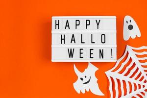 concepto de Halloween. decoraciones festivas - fantasmas de papel y telaraña sobre fondo naranja. foto