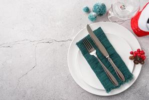 Christmas table setting with white dishware, silverware and red and green decorations on white wooden background. Top view. photo