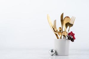 Set of cutlery of spoons, knives and forks in cup with holiday decorations on dining table, copy space photo