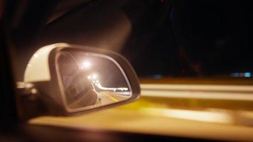 vista del espejo lateral de un coche que conduce rápido por una carretera nocturna en la oscuridad iluminada por farolillos. concepto de vehículo de paseo.