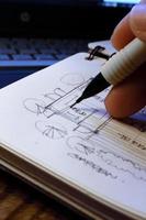 Architect's hands are sketching architectural plans with pencils on a sketchbook on a desk with a laptop. photo