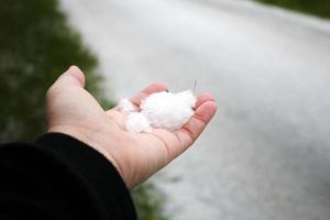 la mano de un hombre sosteniendo nieve en su mano después de que nieva contra un camino cubierto de nieve en el fondo. foto