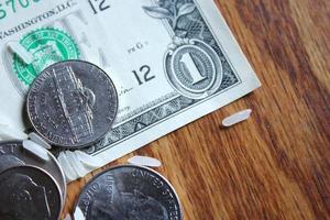las monedas de dólar y los billetes de dólar están esparcidos sobre una mesa de madera con granos de arroz. foto