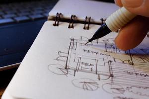 Architect's hands are sketching architectural plans with pencils on a sketchbook on a desk with a laptop. photo